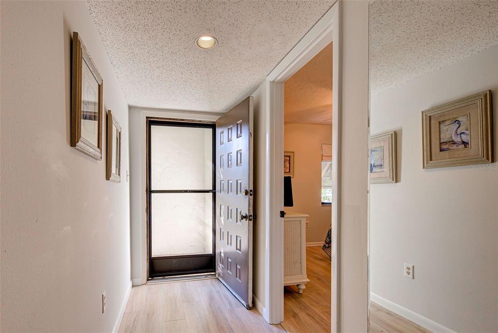A hallway with light wood flooring leads to an open door and an adjacent bedroom — 5179 WILLOW LINKS UNIT 27, SARASOTA, FL