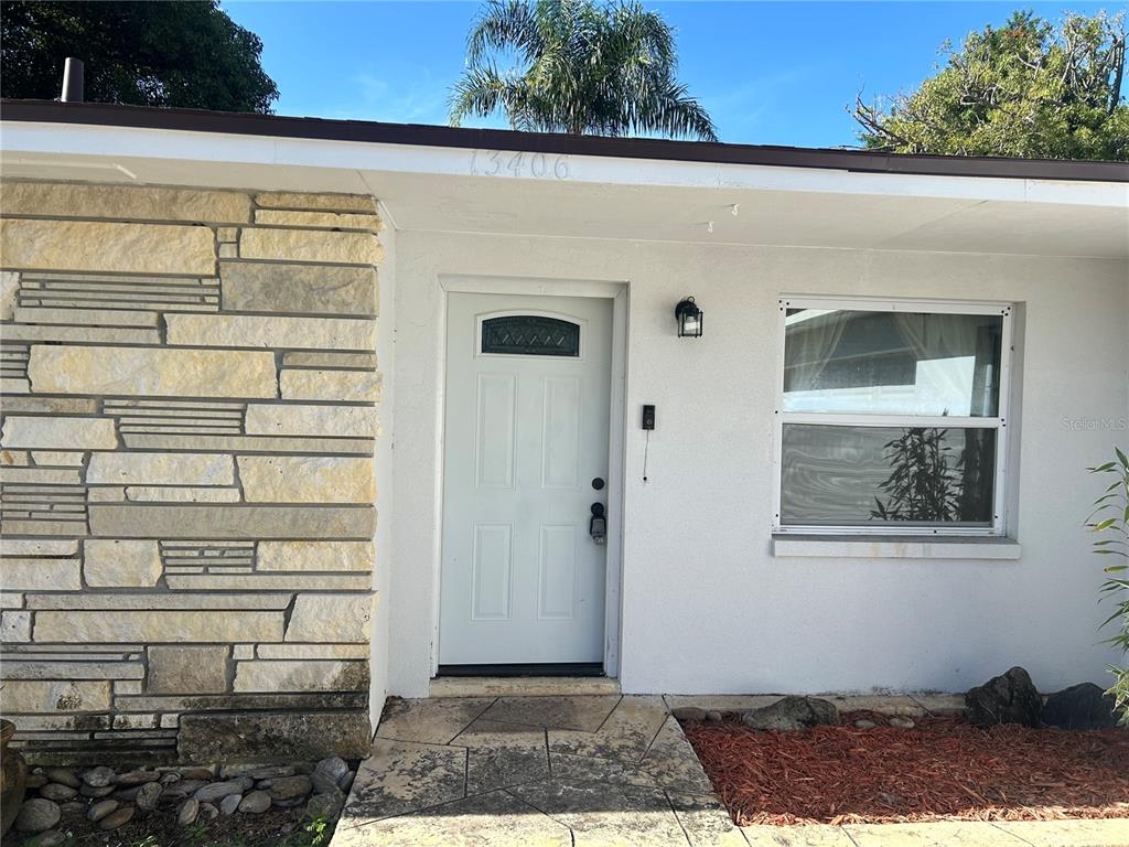 The exterior of a house features a white front door, stone siding, and a window — 13406 BELLEWOOD AVENUE, SEMINOLE, FL