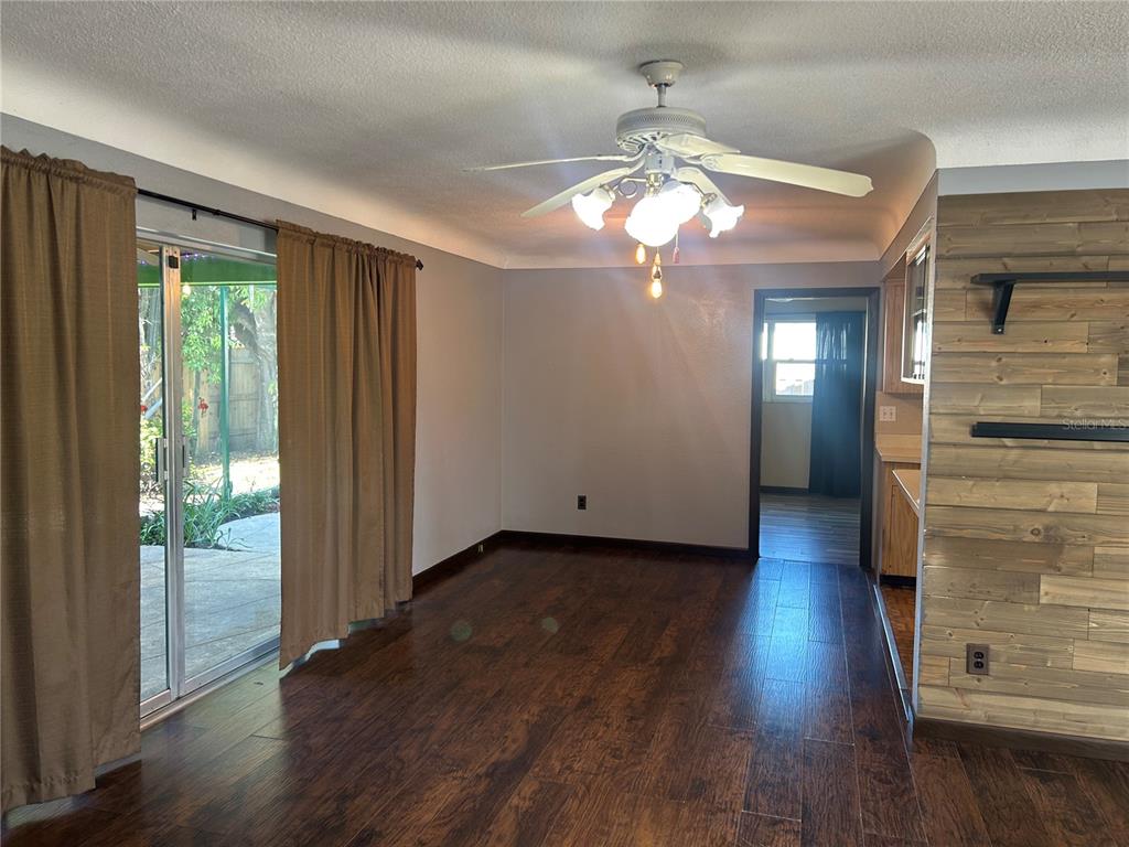 A dining area with wood-look flooring, a ceiling fan, and a wood-paneled accent wall — 13406 BELLEWOOD AVENUE, SEMINOLE, FL