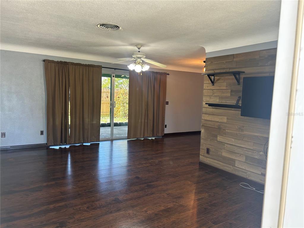 A living room features dark wood-look flooring, a wood-paneled accent wall, and sliding glass doors — 13406 BELLEWOOD AVENUE, SEMINOLE, FL