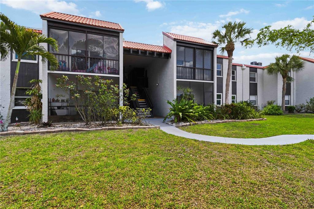 A two-story apartment building features screened balconies, a central staircase, and surrounding palm trees — 3281 BENEVA ROAD UNIT 104, SARASOTA, FL