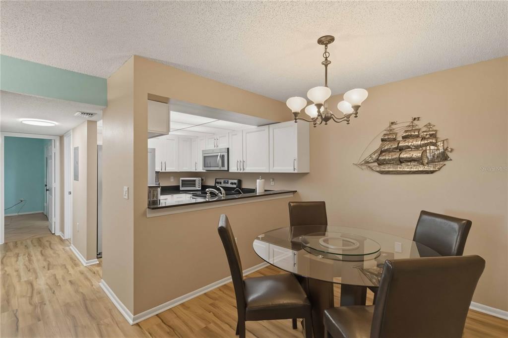 A dining area with a glass table and chairs sits adjacent to an open kitchen — 3281 BENEVA ROAD UNIT 104, SARASOTA, FL