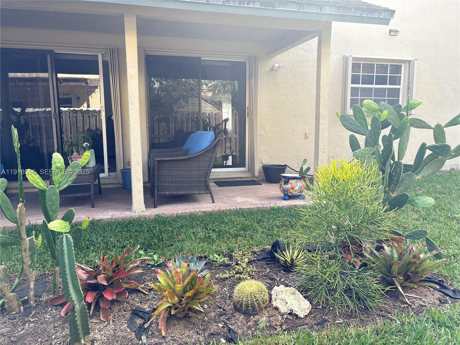 A patio with sliding glass doors overlooks a garden featuring various cacti and succulents — 7809 NW 192nd St, Hialeah FL 33015, HIALEAH, FL