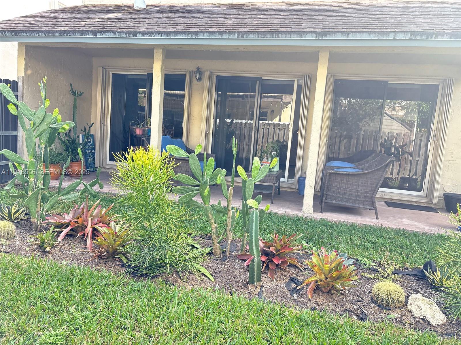 A patio with sliding glass doors features a garden bed with various cacti and bromeliads — 7809 NW 192nd St, Hialeah FL 33015, HIALEAH, FL