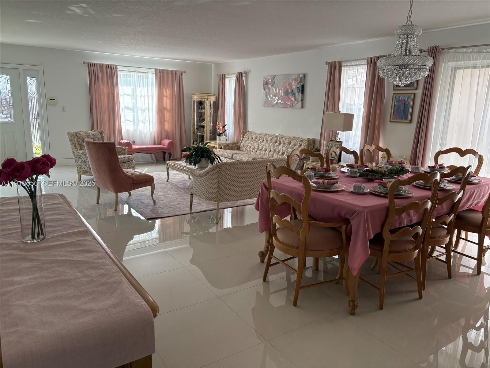 A bright, open-concept living and dining room features tile floors, pink curtains, and traditional furniture — 7809 NW 192nd St, Hialeah FL 33015, HIALEAH, FL