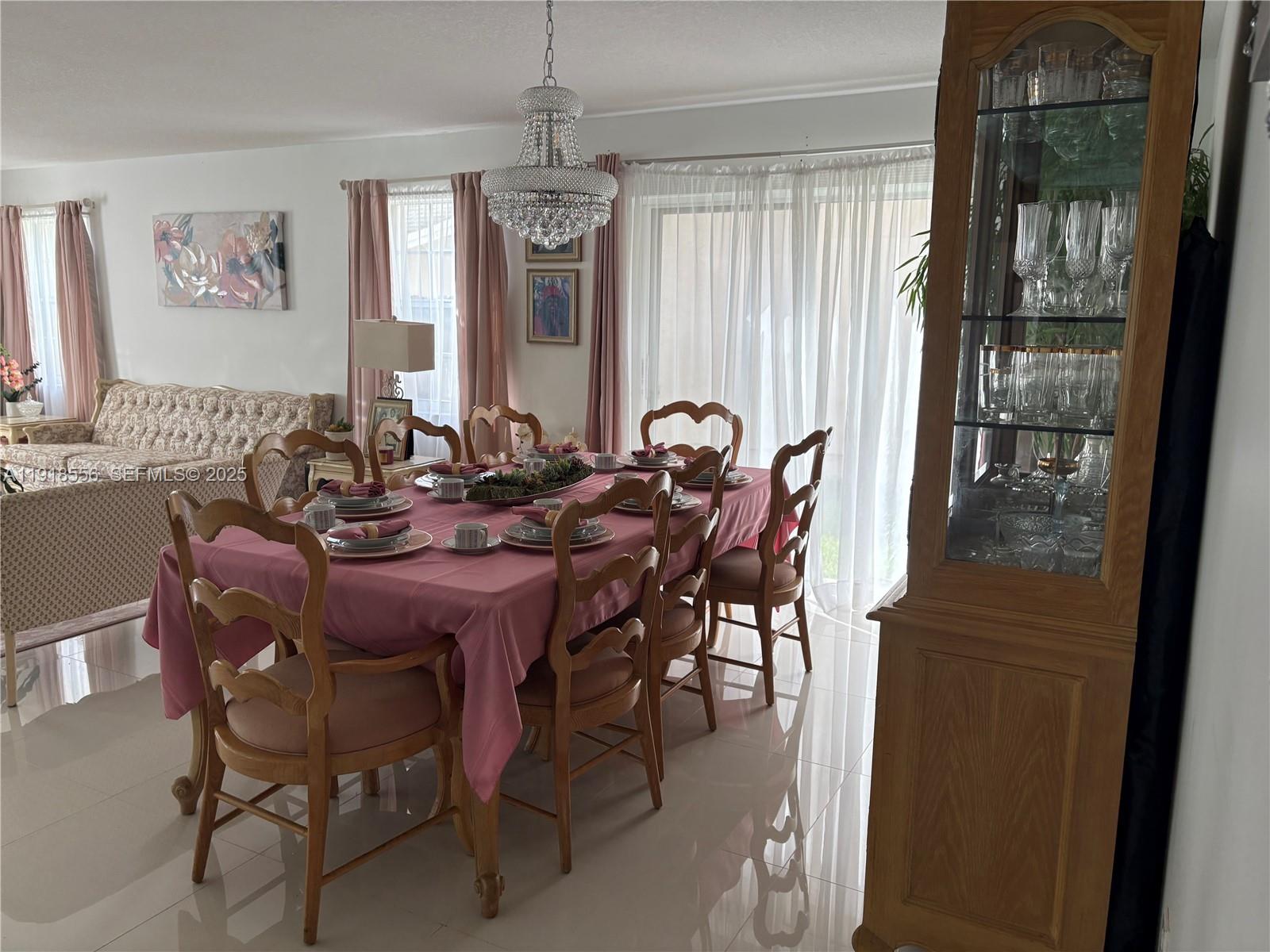 A dining room features a pink-clothed table, wooden chairs, a crystal chandelier, and a hutch — 7809 NW 192nd St, Hialeah FL 33015, HIALEAH, FL