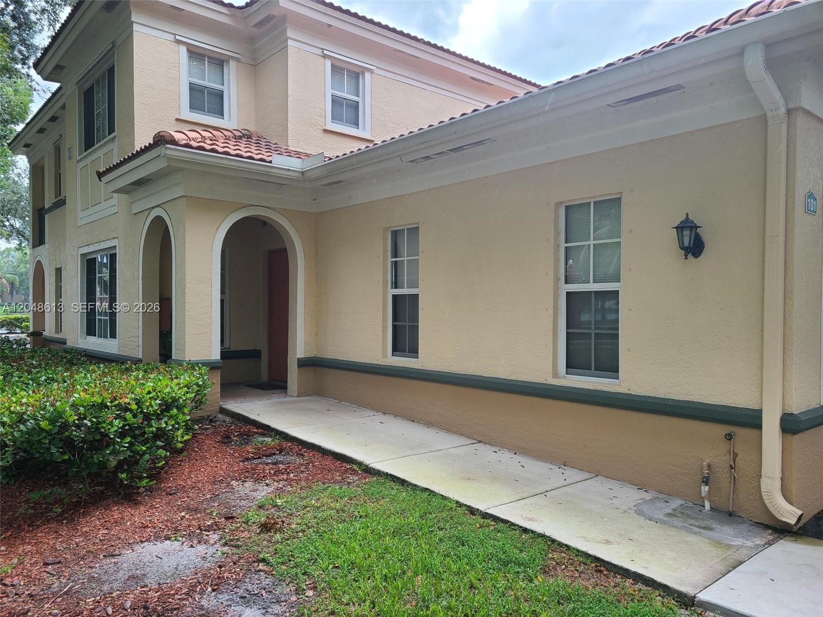 The exterior of a two-story tan building features a covered entryway and a concrete walkway — 2541 Centergate Dr # 101, Miramar FL 33025, MIRAMAR, FL