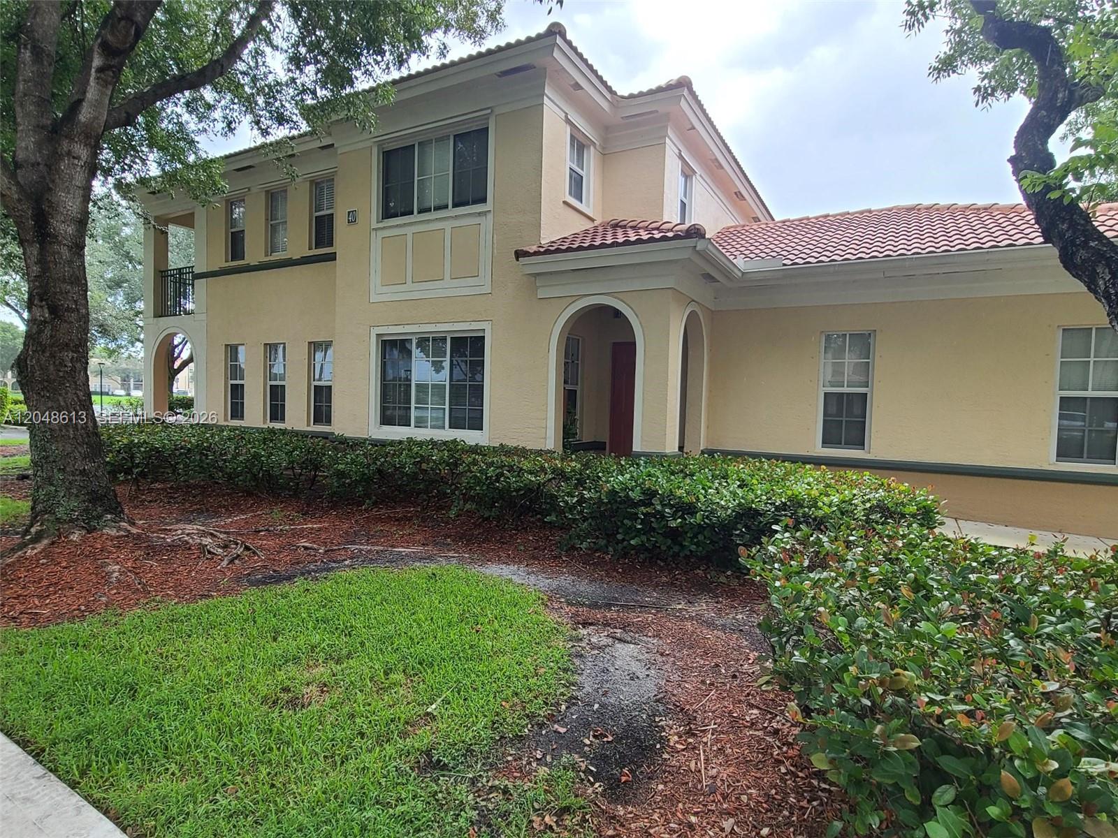 A two-story tan stucco building features a tiled roof, arched entryway, and landscaped front yard — 2541 Centergate Dr # 101, Miramar FL 33025, MIRAMAR, FL
