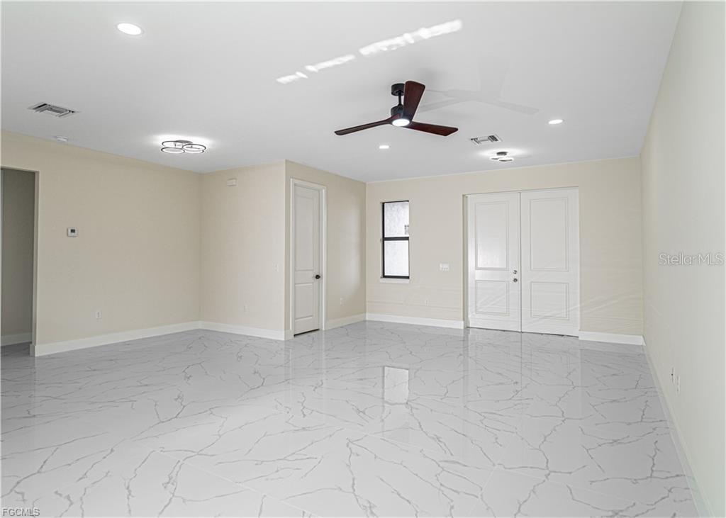 A bright, empty room features white marble-patterned tile flooring, a ceiling fan, and double doors — 3701 28TH STREET SW, LEHIGH ACRES, FL