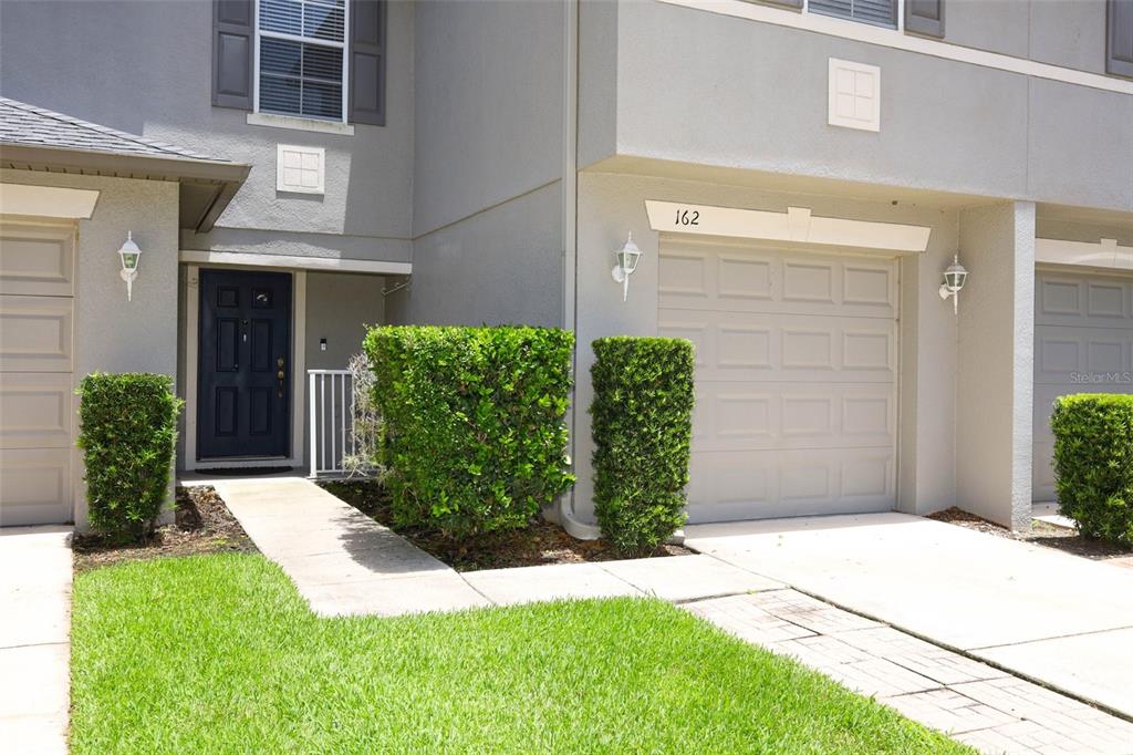 A gray two-story townhouse exterior features a dark front door, a garage, and manicured hedges — 162 CONSTITUTION WAY, WINTER SPRINGS, FL