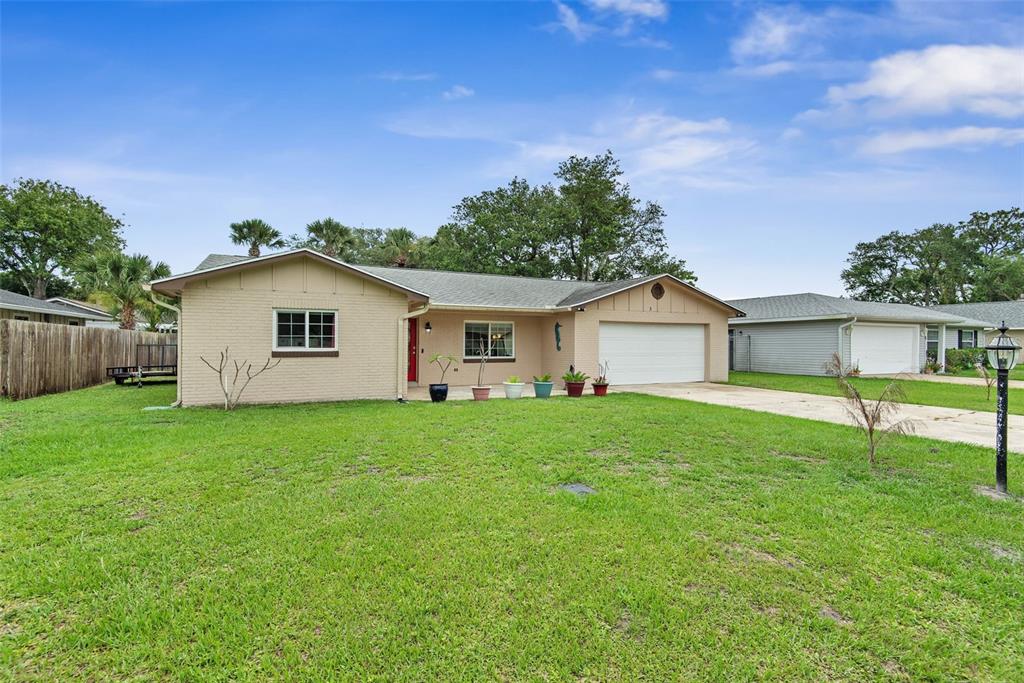 A single-story tan brick house with a white garage door and a red front door — 3 OVERBROOK COURT, ORMOND BEACH, FL