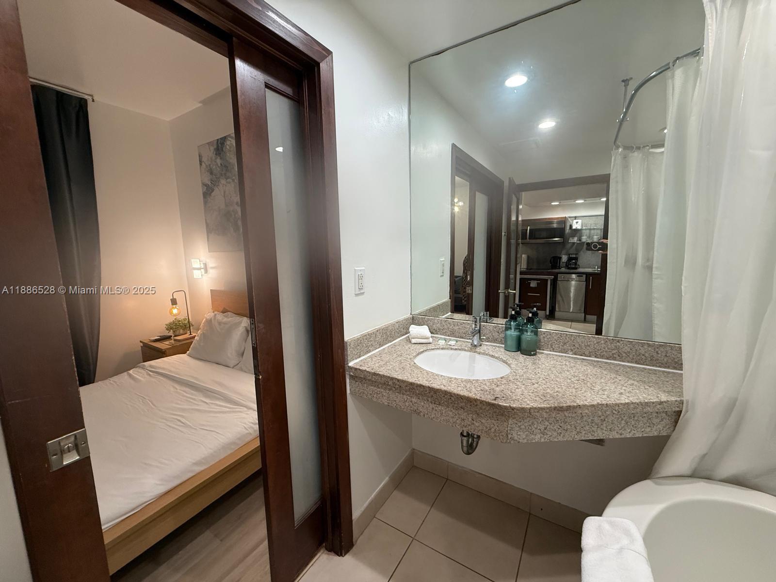 A bathroom with a granite vanity and mirror opens into a bedroom with a bed — 1036 Ocean Dr # B303, Miami Beach FL 33139, MIAMI BEACH, FL