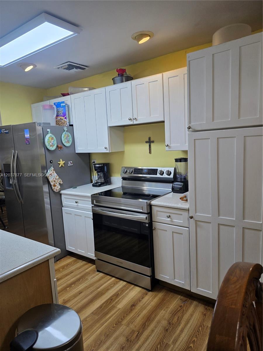 A kitchen features white cabinets, stainless steel appliances, and light wood-look flooring — 19500 SW 87th Ave, Cutler Bay FL 33157, CUTLER BAY, FL