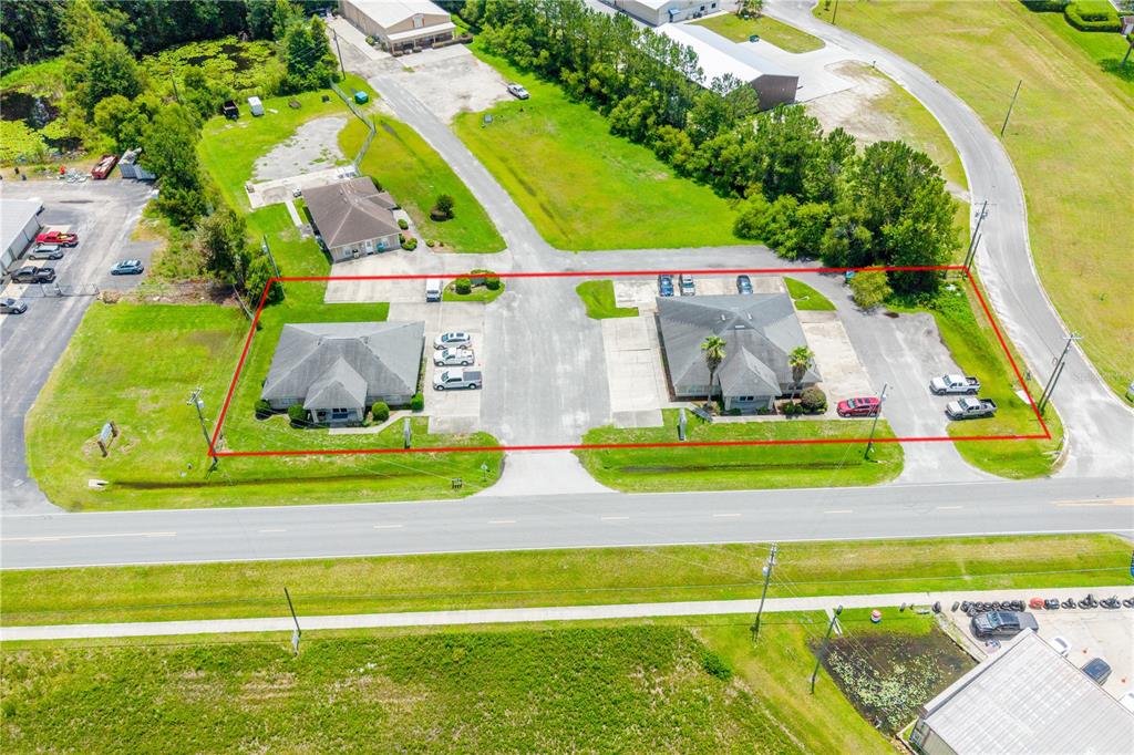 An aerial view shows two commercial buildings with parking lots enclosed by a red boundary line — 853 SW SISTERS WELCOME ROAD, LAKE CITY, FL