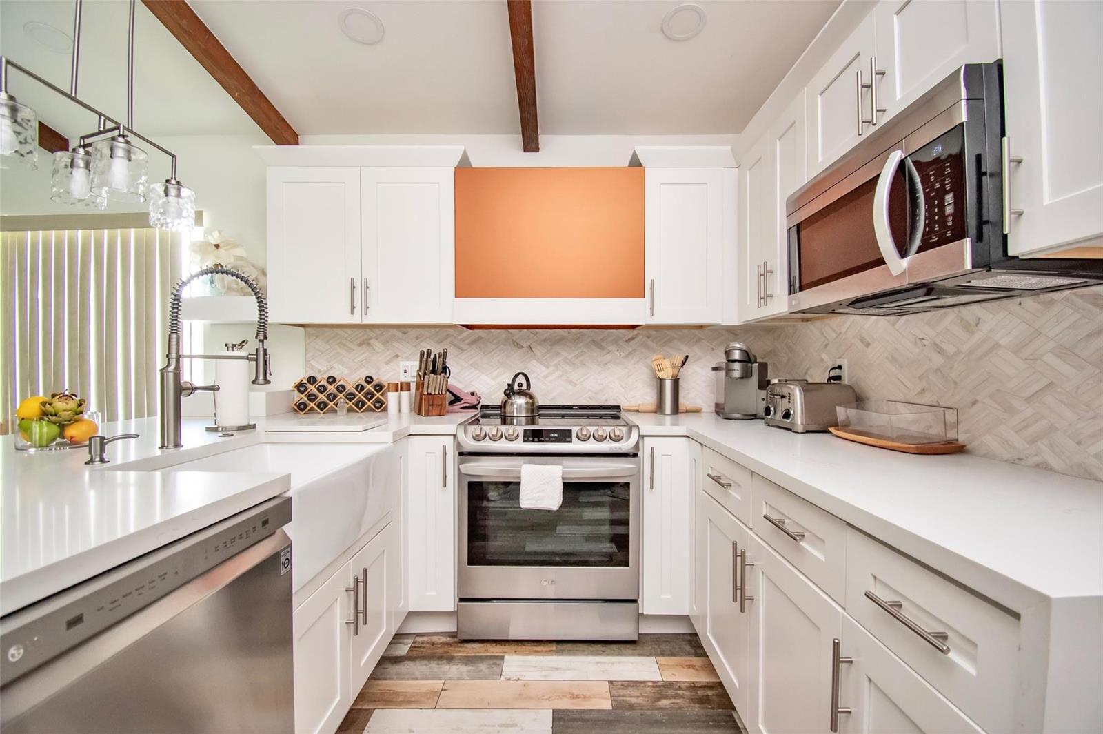 A modern kitchen features white cabinets, stainless steel appliances, a herringbone backsplash, and wood beams — 6557 Country Wood Way, Delray Beach FL 33484, DELRAY BEACH, FL