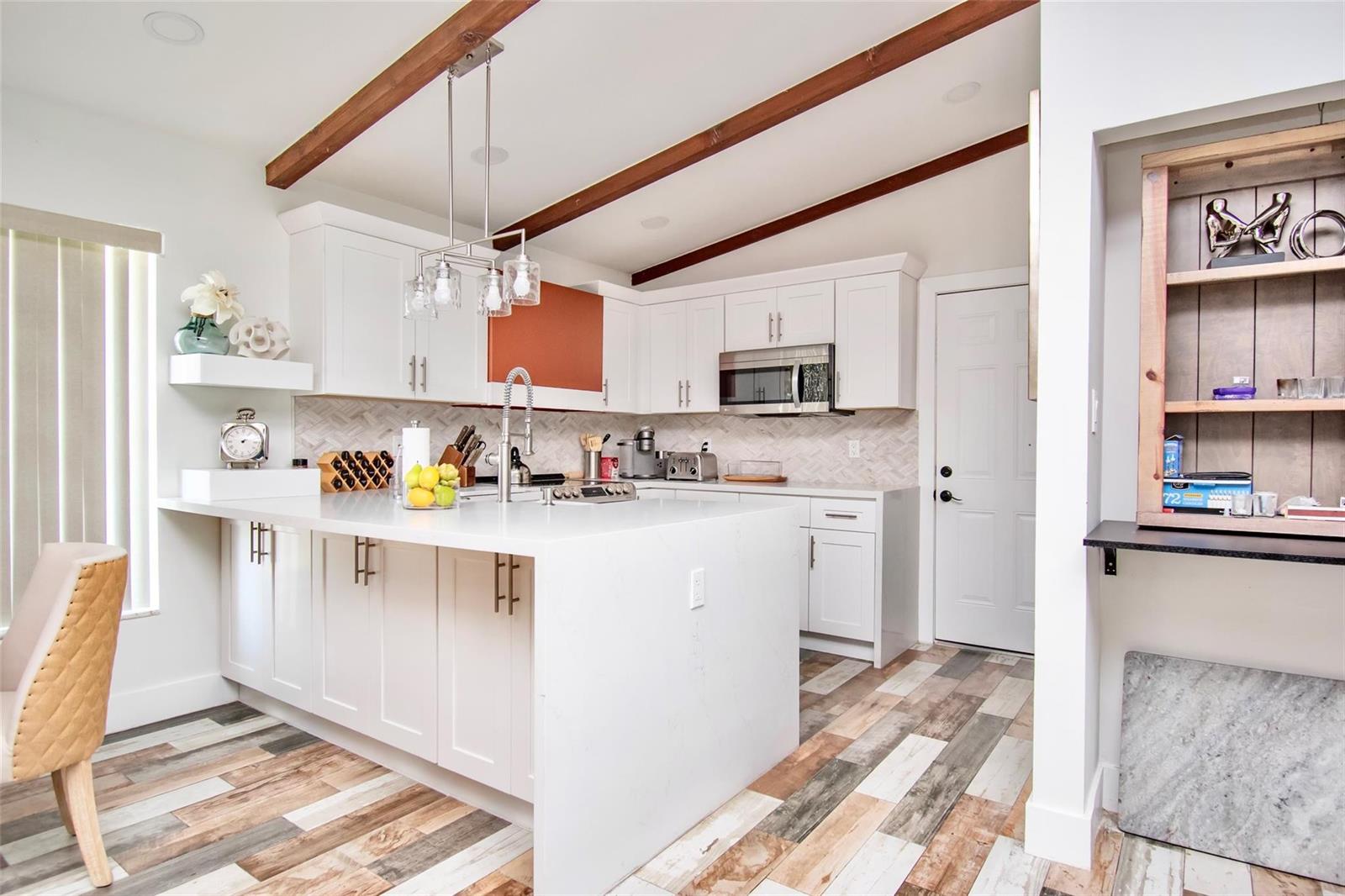 A modern kitchen features white cabinetry, a large quartz island, and wood-look plank flooring — 6557 Country Wood Way, Delray Beach FL 33484, DELRAY BEACH, FL
