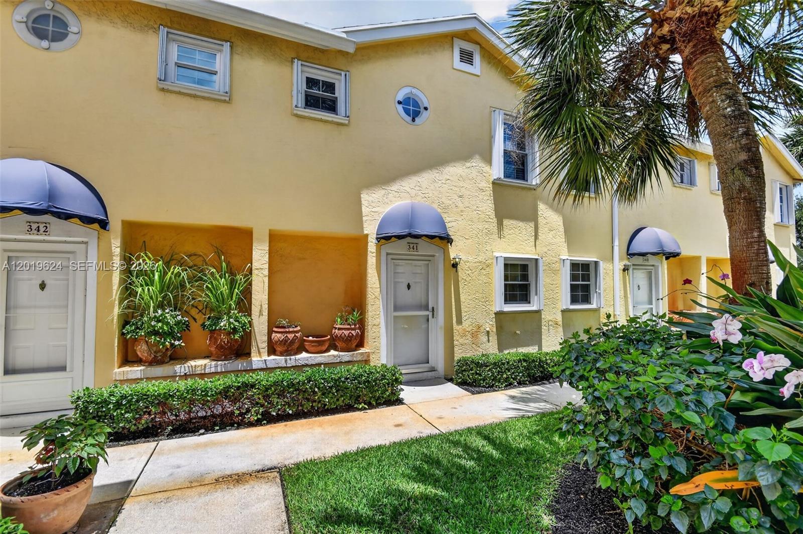 A row of yellow townhouses features blue awnings, arched windows, and potted plants — 341 Waterside Dr # 341, Hypoluxo FL 33462, HYPOLUXO, FL
