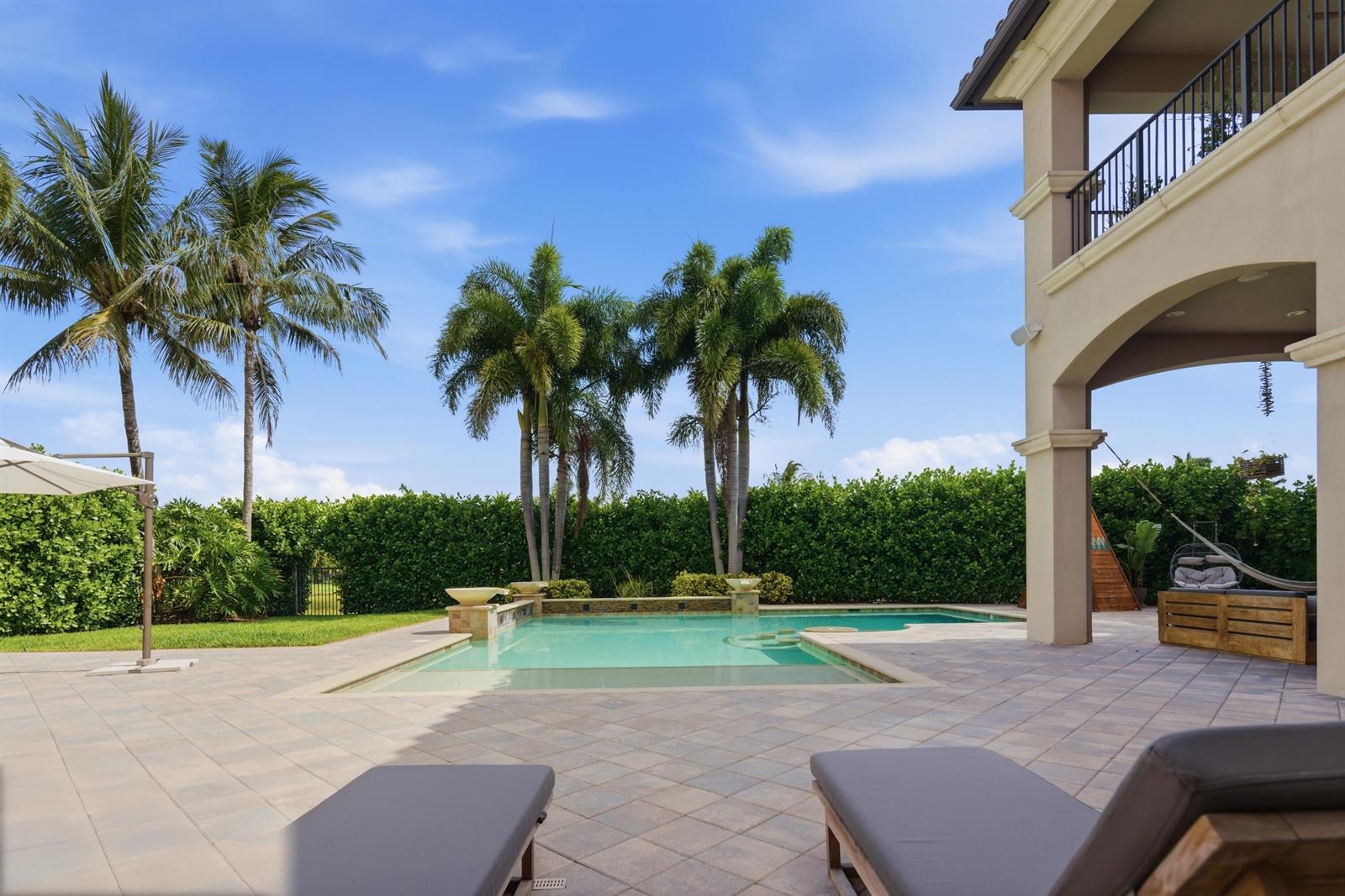 A backyard patio features a swimming pool, lounge chairs, palm trees, and a hedge fence — 16907 Crown Bridge Drive, Delray Beach FL 33446, DELRAY BEACH, FL