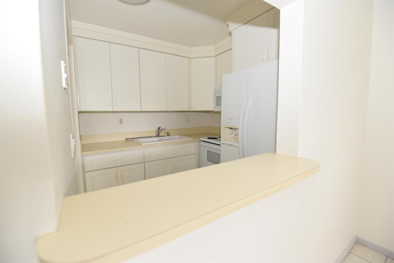 A kitchen features white cabinets, a white refrigerator, and a beige countertop with a sink — 164 Andover G, West Palm Beach FL 33417, WEST PALM BEACH, FL