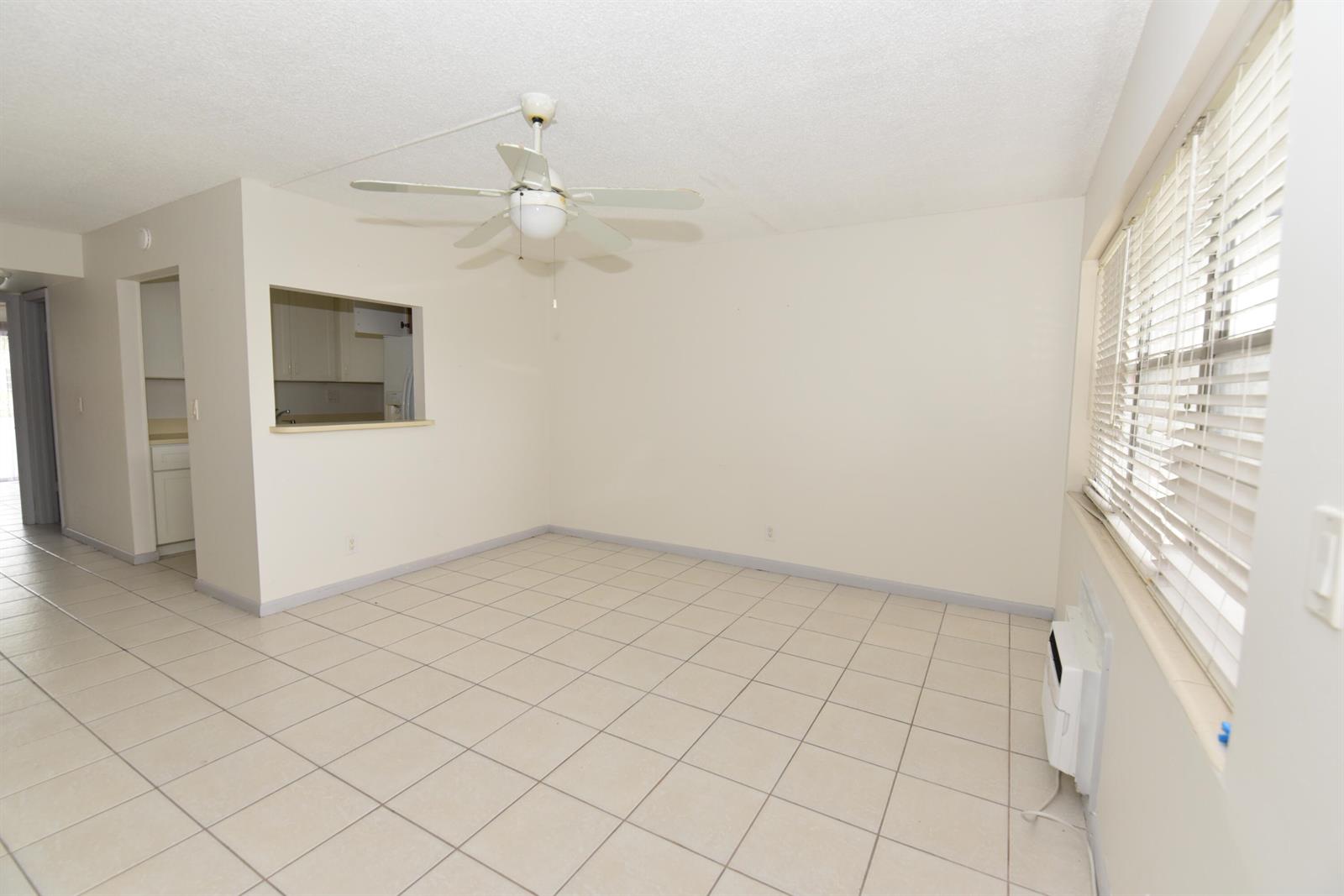 An empty living room features white tile floors, a ceiling fan, and a kitchen pass-through — 164 Andover G, West Palm Beach FL 33417, WEST PALM BEACH, FL