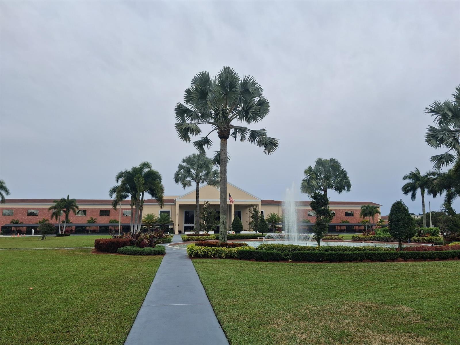 A paved walkway leads toward a building with a fountain and palm trees in front — 105 Suffolk C # 105, Boca Raton FL 33434, BOCA RATON, FL