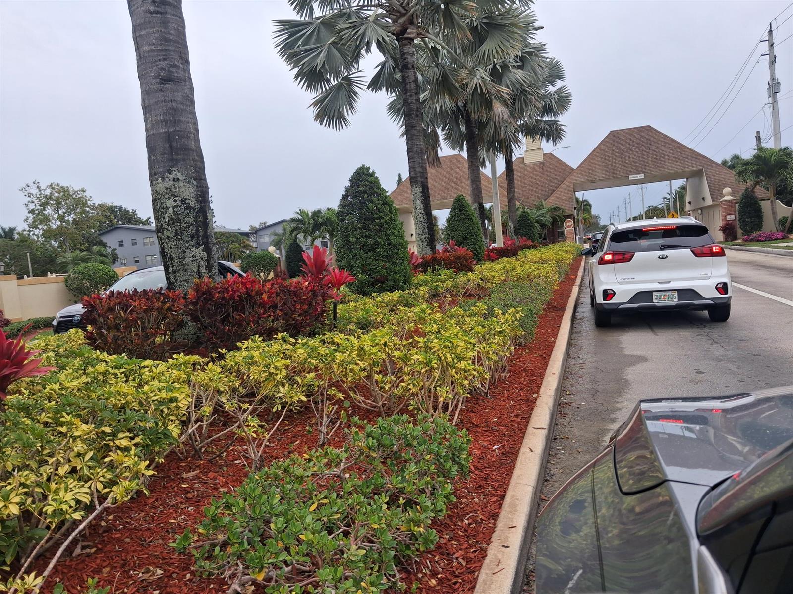 A white car waits in a line of traffic at a gated community entrance — 105 Suffolk C # 105, Boca Raton FL 33434, BOCA RATON, FL