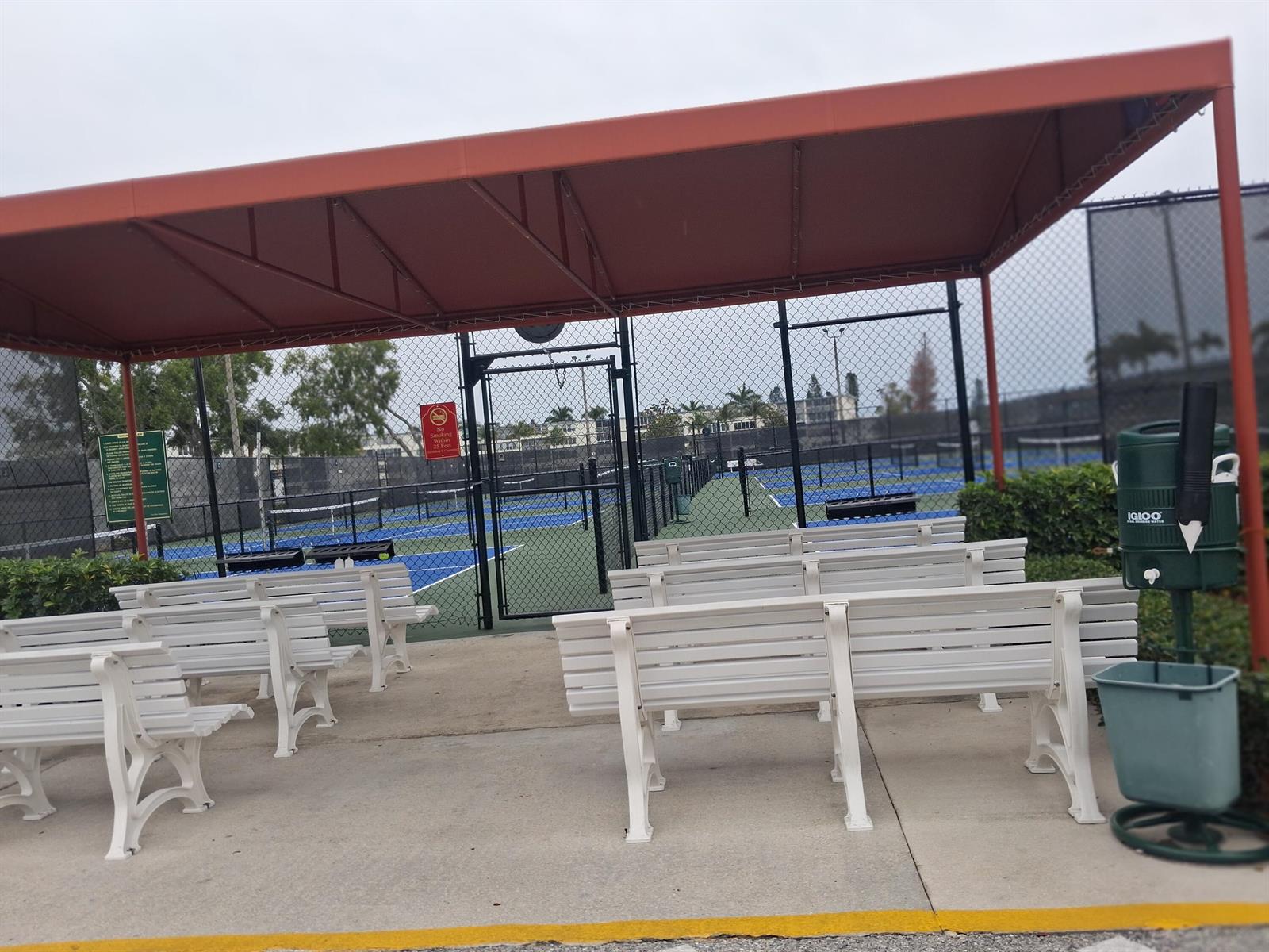 A covered outdoor seating area with white benches overlooks fenced pickleball courts — 105 Suffolk C # 105, Boca Raton FL 33434, BOCA RATON, FL