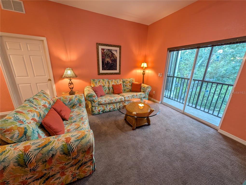 A living room features floral sofas, a glass-topped coffee table, and sliding glass balcony doors — 210 WATLING WAY UNIT 24-210, DAVENPORT, FL