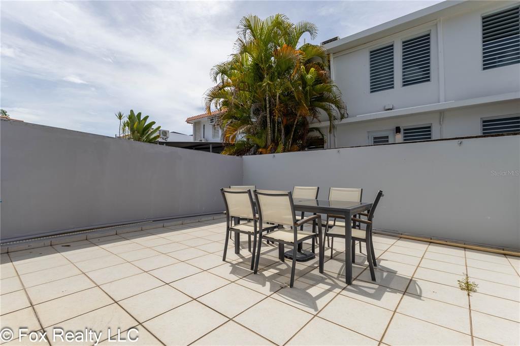 A patio with a dining set is enclosed by a gray wall near a building — B4 URB VISTA AZUL, RINCON, PR