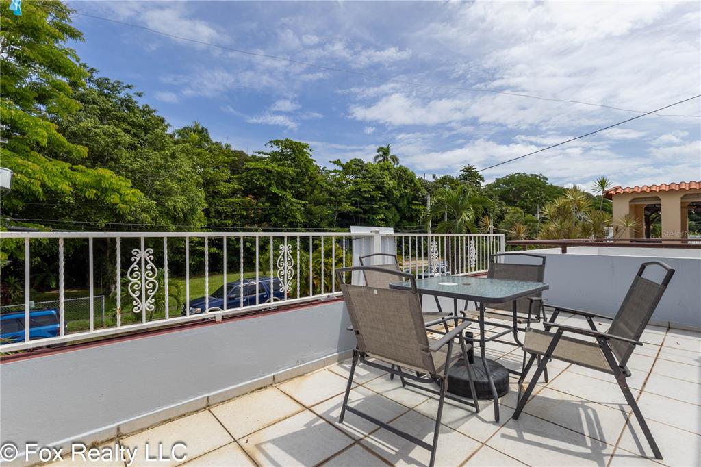 An outdoor balcony features a glass-topped table with four chairs and a white metal railing — B4 URB VISTA AZUL, RINCON, PR
