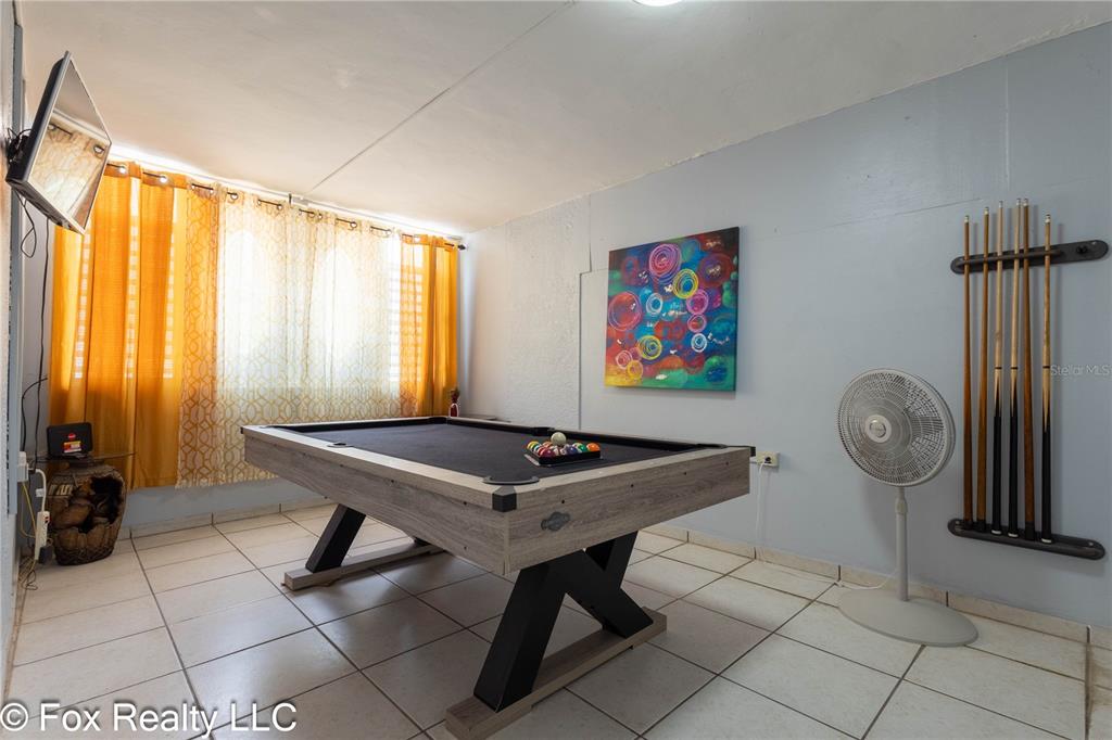 A game room features a pool table, wall-mounted cues, a fan, and yellow curtains — B4 URB VISTA AZUL, RINCON, PR