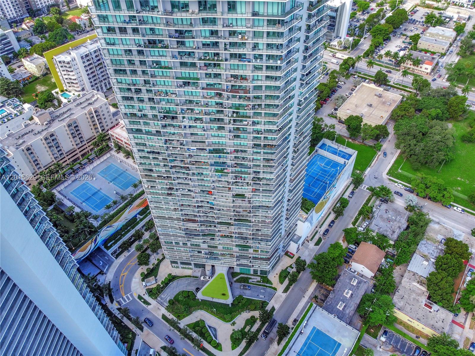 An aerial view shows a tall residential skyscraper surrounded by tennis courts and urban streets — 501 NE 31st St # 608, Miami FL 33137, MIAMI, FL