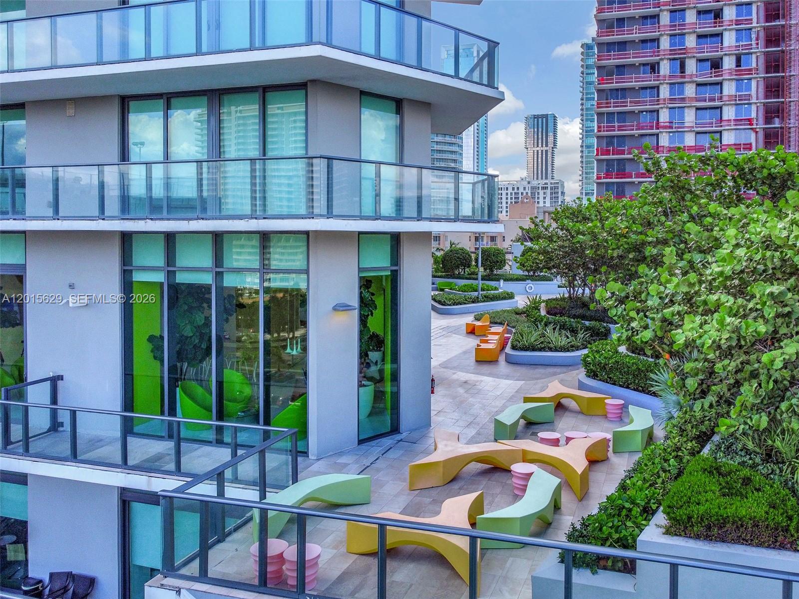 An outdoor terrace features modern, colorful sculptural seating and landscaping next to a glass-walled building — 501 NE 31st St # 608, Miami FL 33137, MIAMI, FL