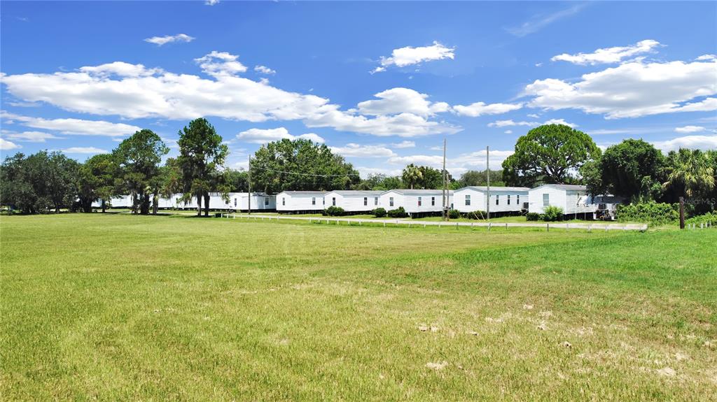A row of white mobile homes sits behind a large, open grassy field under a sky — 6304 EUGENE ACRES LANE, GIBSONTON, FL