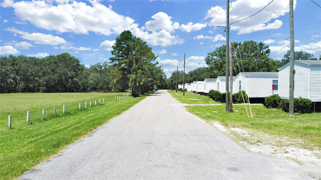 A paved road runs between a grassy field and a row of white mobile homes — 6304 EUGENE ACRES LANE, GIBSONTON, FL