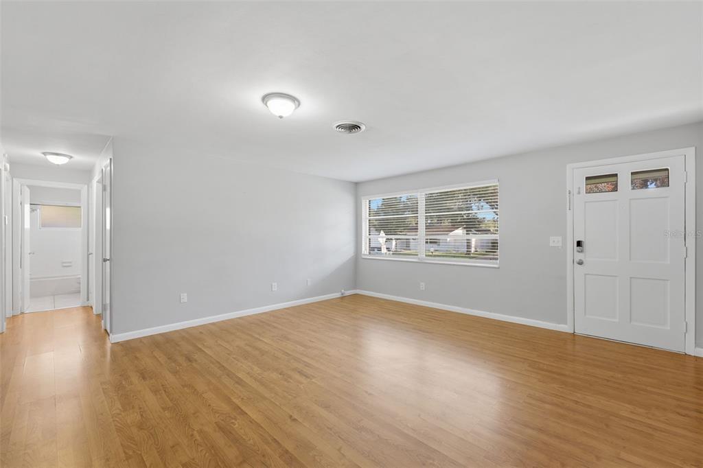 An empty living room features light gray walls, hardwood flooring, a window, and a front door — 1387 BELLEVUE BOULEVARD, CLEARWATER, FL