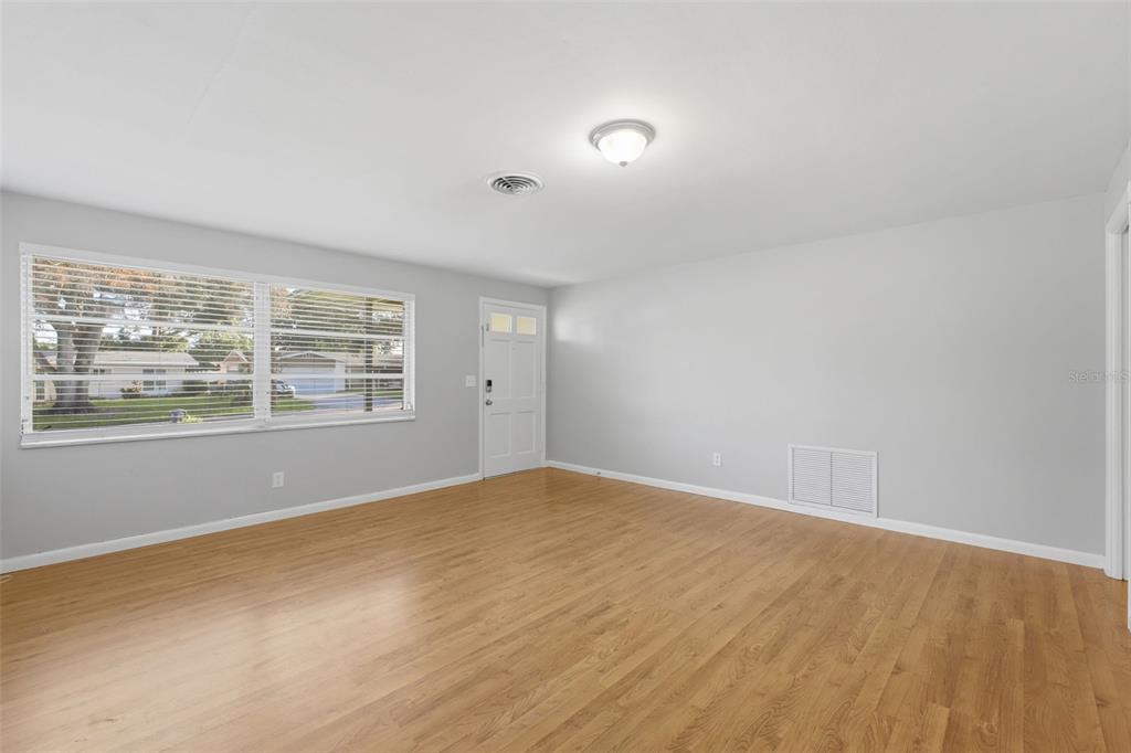 An empty room with light wood flooring, gray walls, a large window, and a door — 1387 BELLEVUE BOULEVARD, CLEARWATER, FL