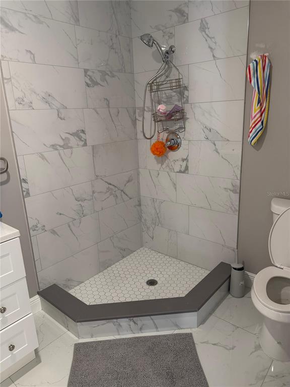 A bathroom features a corner shower with marble-look tile walls and a hexagonal tile floor — 5950 HIGH STREET, NEW PORT RICHEY, FL