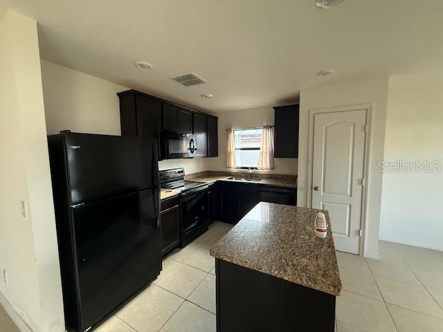 A kitchen features dark cabinets, granite countertops, a kitchen island, and a black refrigerator — 1884 AMBER SWEET CIRCLE, DUNDEE, FL