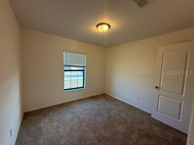 An empty bedroom features beige walls, brown carpet, a single window, and a white door — 1884 AMBER SWEET CIRCLE, DUNDEE, FL