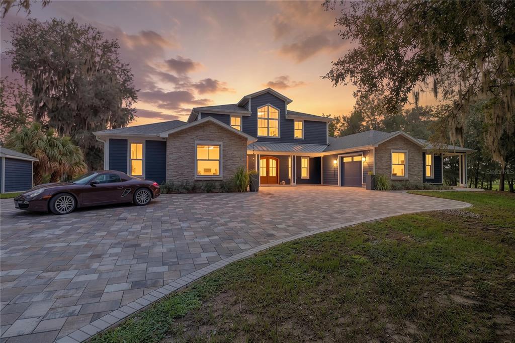 A two-story house with blue siding, stone accents, and a paved driveway at sunset — 25198 LILY PAD LANE, BROOKSVILLE, FL