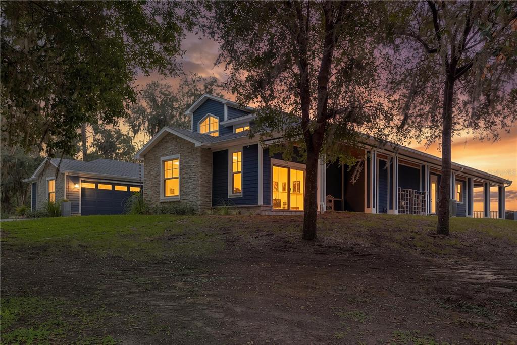A blue house with stone accents and a detached garage at sunset — 25198 LILY PAD LANE, BROOKSVILLE, FL