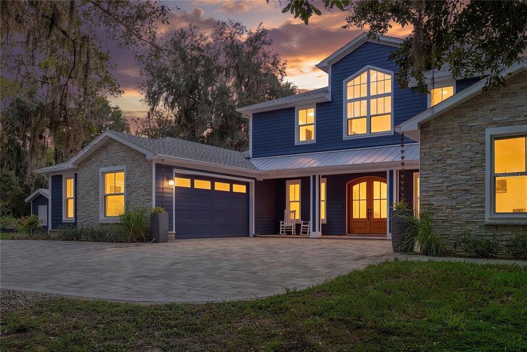 A two-story blue house with stone siding, a paved driveway, and a garage at dusk — 25198 LILY PAD LANE, BROOKSVILLE, FL