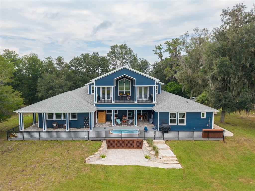 A blue two-story house with a deck, swimming pool, and stone patio in the backyard — 25198 LILY PAD LANE, BROOKSVILLE, FL