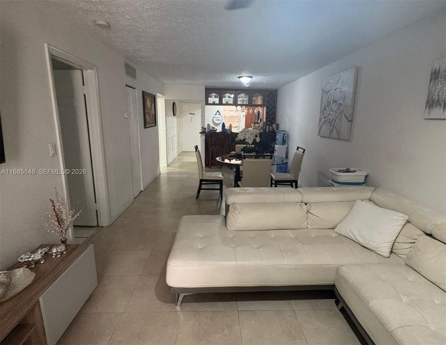 A living room with a white sectional sofa, tiled floors, and an adjacent dining area — 6055 W 19th Ave # 318, Hialeah FL 33012, HIALEAH, FL