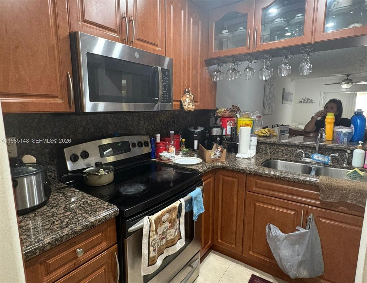 A kitchen features wood cabinets, granite countertops, stainless steel appliances, and a hanging glass rack — 6055 W 19th Ave # 318, Hialeah FL 33012, HIALEAH, FL