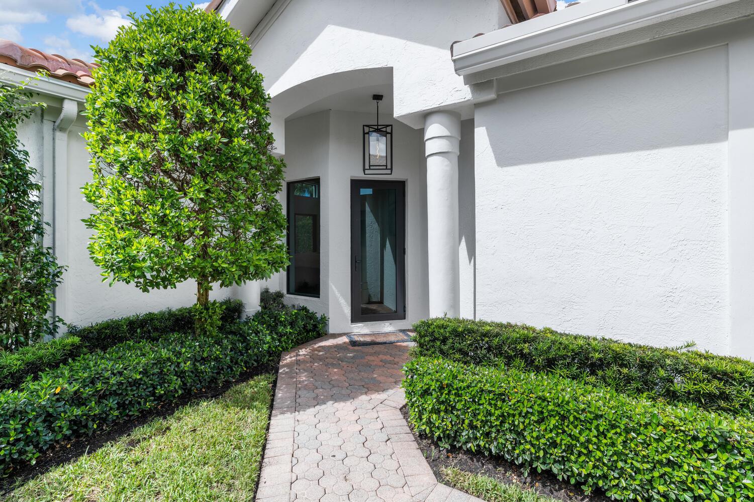 A paved walkway leads to the front entrance of a white house with landscaping — 12618 Mallet Circle, Wellington FL 33414, WELLINGTON, FL