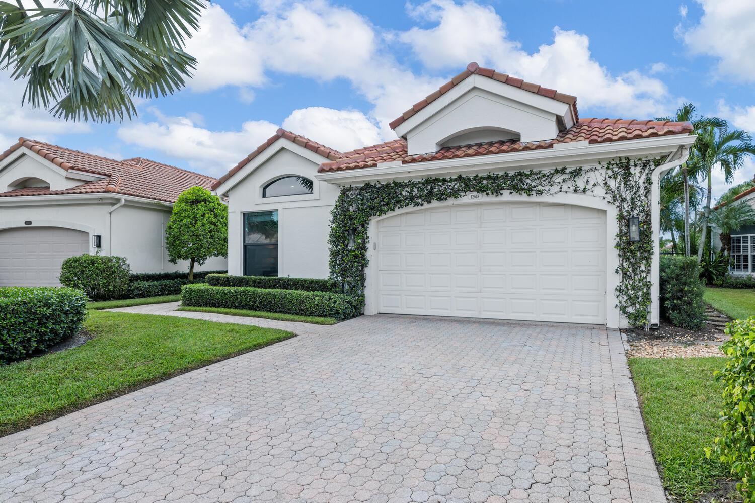 A white stucco house with a tiled roof and a paved driveway under a blue sky — 12618 Mallet Circle, Wellington FL 33414, WELLINGTON, FL