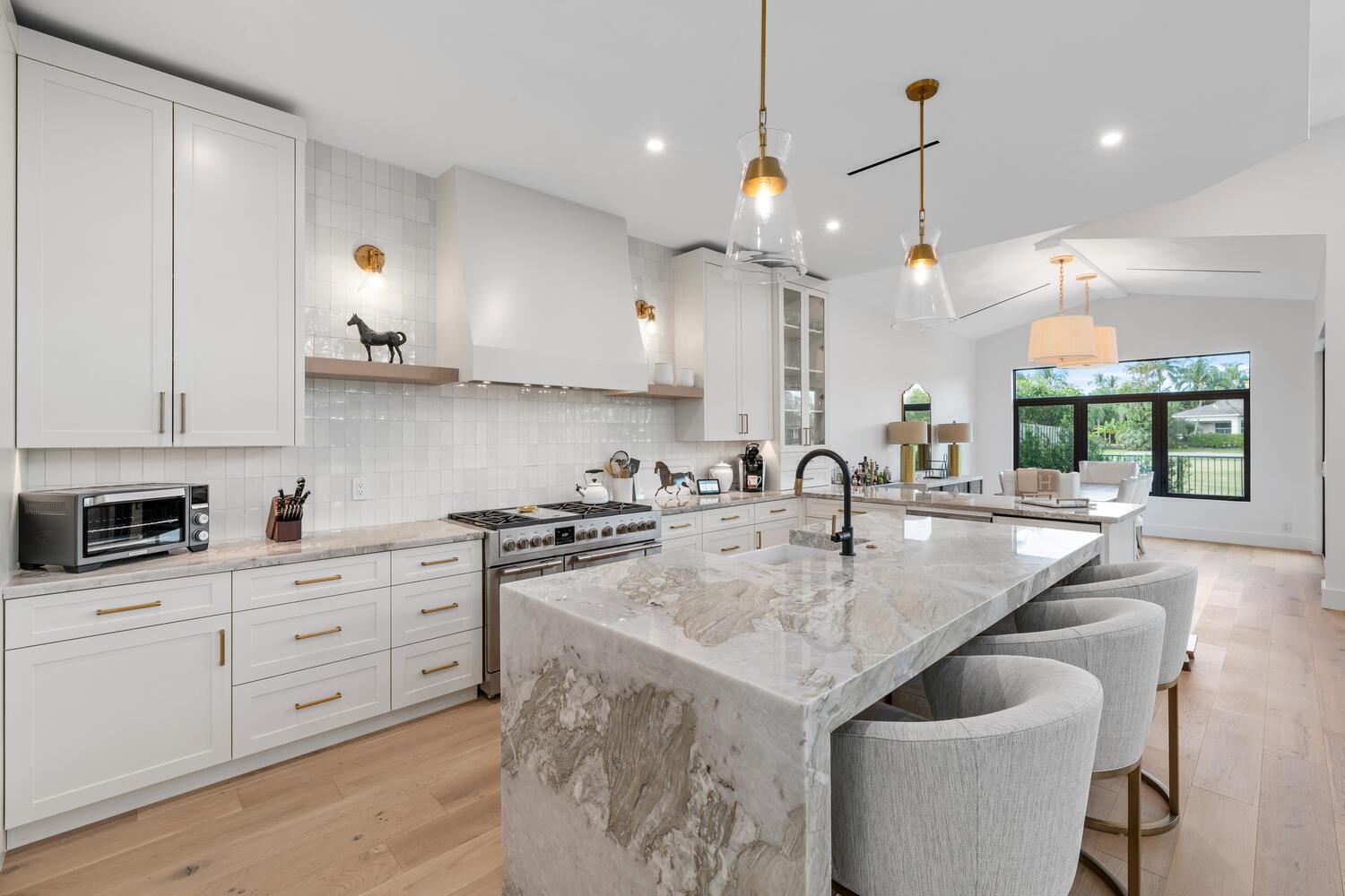 A modern kitchen features white cabinetry, a large marble island, and light wood flooring — 12618 Mallet Circle, Wellington FL 33414, WELLINGTON, FL