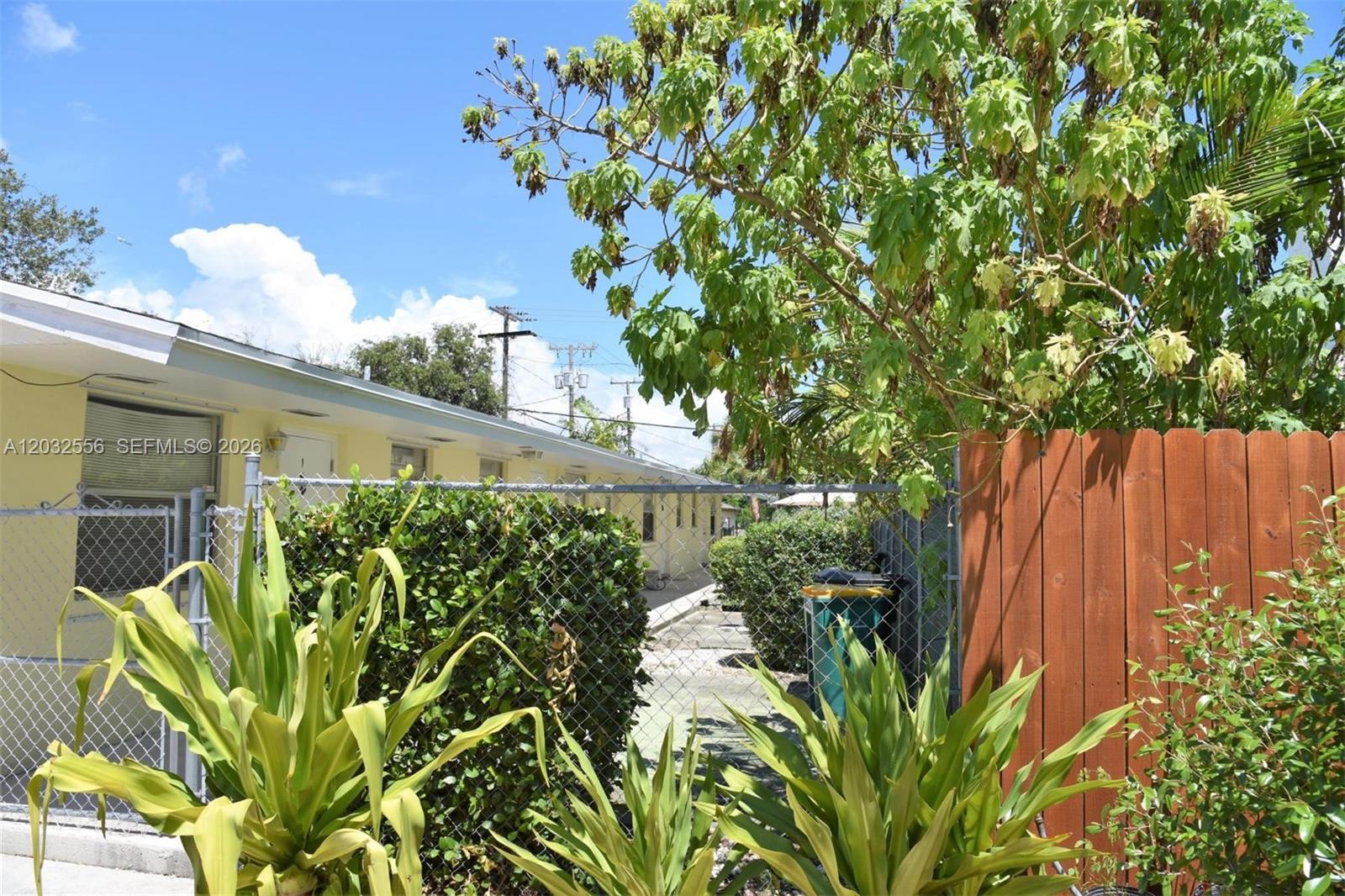 A yellow building exterior is visible behind a chain-link fence and green landscaping — 1008 N 18  AVENUE, Lake Worth FL 33460, LAKE WORTH, FL